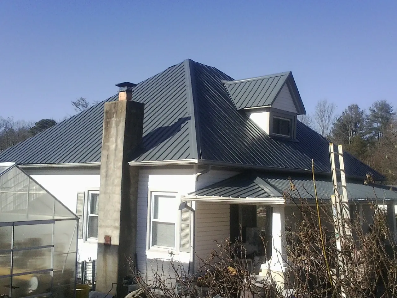 Dark blue standing seam metal roof on a white farmhouse with dormer — Slate & Tile Roof Repair by Roofing Brothers in Conrad