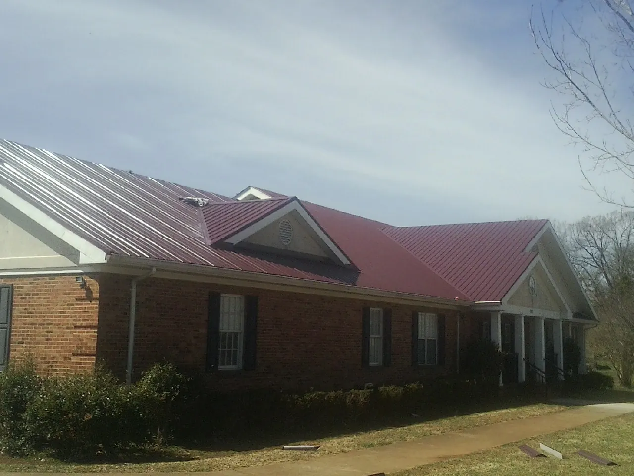 Red metal roof with gabled entries on a long brick building, from a Hail Damage Roof Repair job in Conrad
