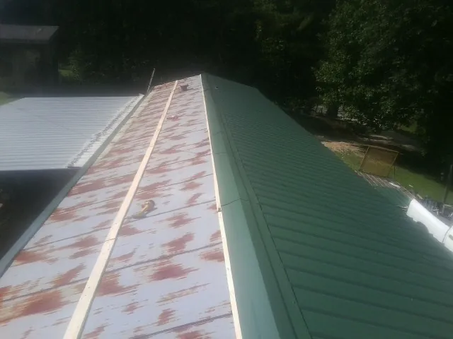 Old rusted panels beside newly installed green metal roofing — Wind Damage Roof Repair by Roofing Brothers in Conrad