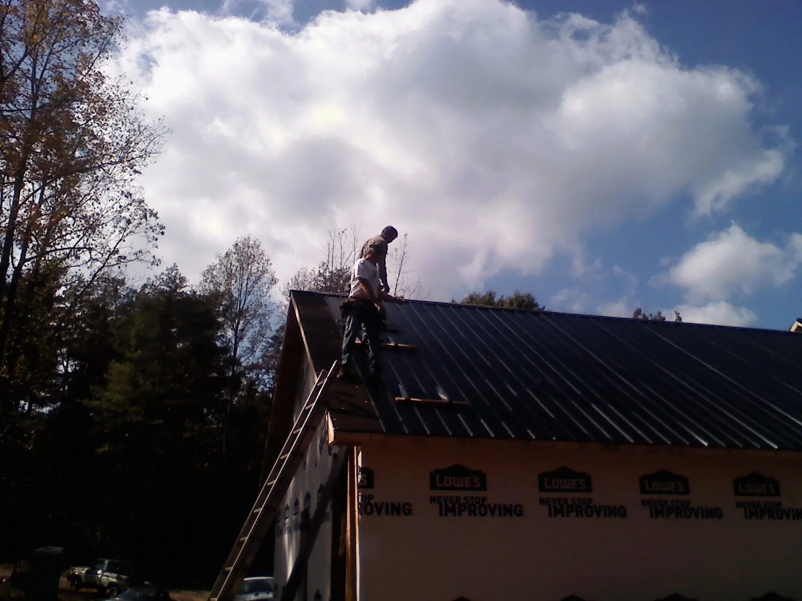 Roofer fastening dark metal panels high against a cloudy sky, from a Roof Inspection job in Conrad