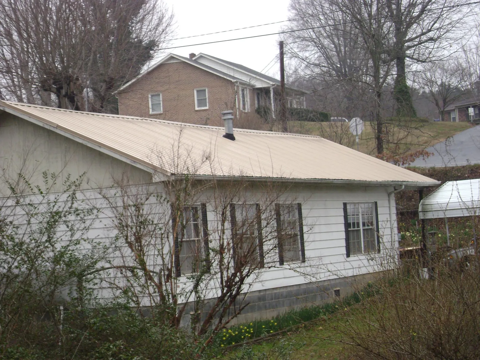 Tan metal roof on a white sided house set into a hillside — Commercial Roofing by Roofing Brothers in Conrad