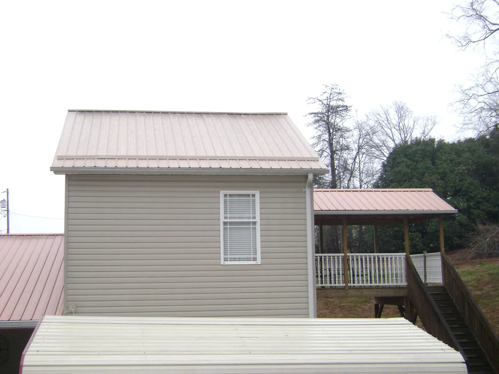 Tan metal roofs on a two story addition and attached porch, from a Roof Replacement job in Conrad